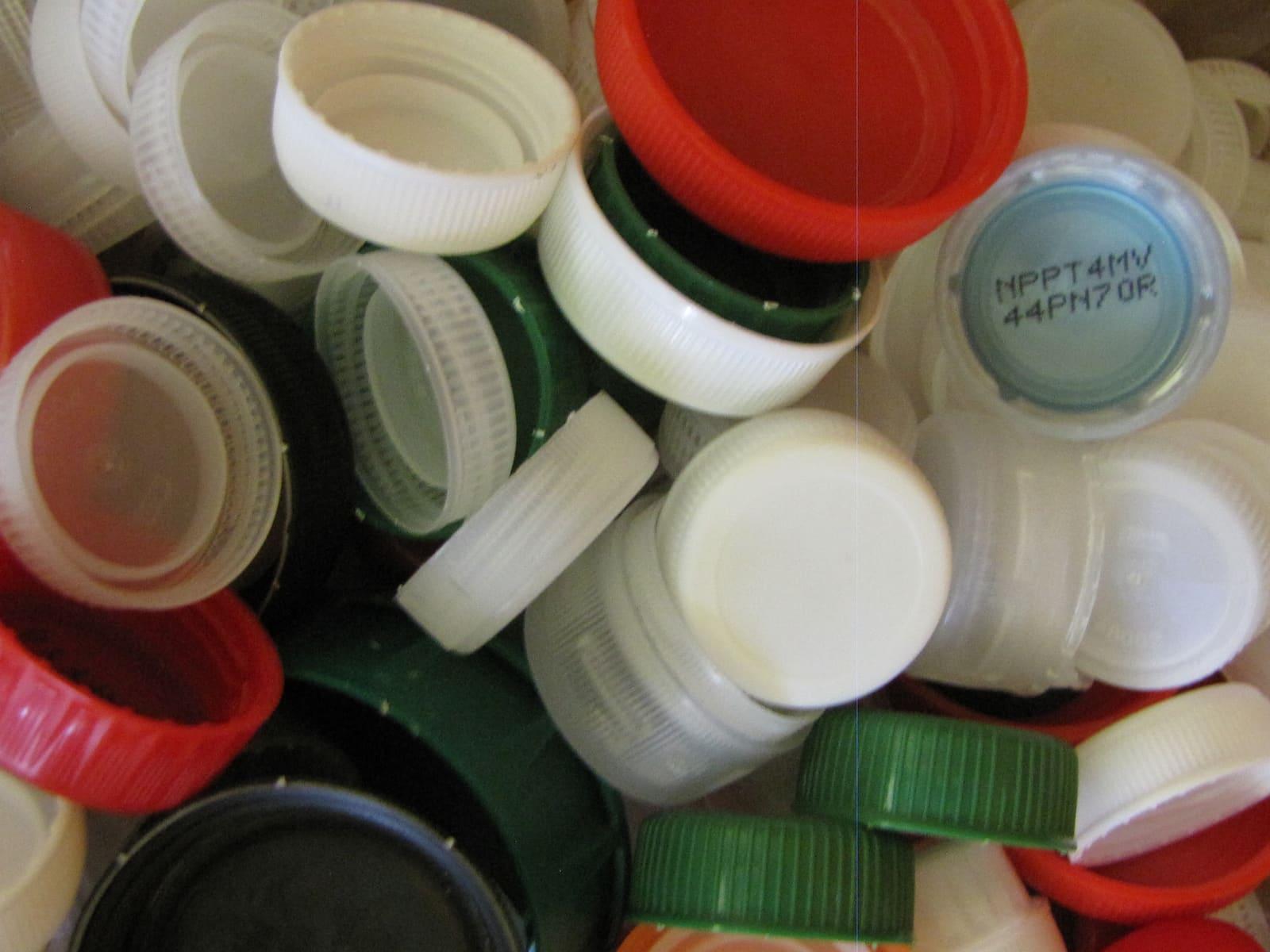 A close-up pile of used plastic bottle lids in white, red, green and blue