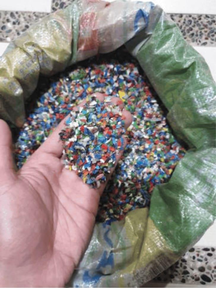 A hand holding multicoloured shredded HDPE flakes above a full sack